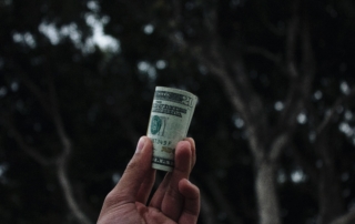 hand holding a roll of money showing a $20 bill