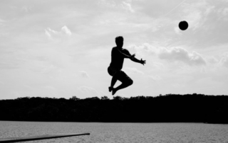 man jumping into lake reaching out to catch a ball as he's going down