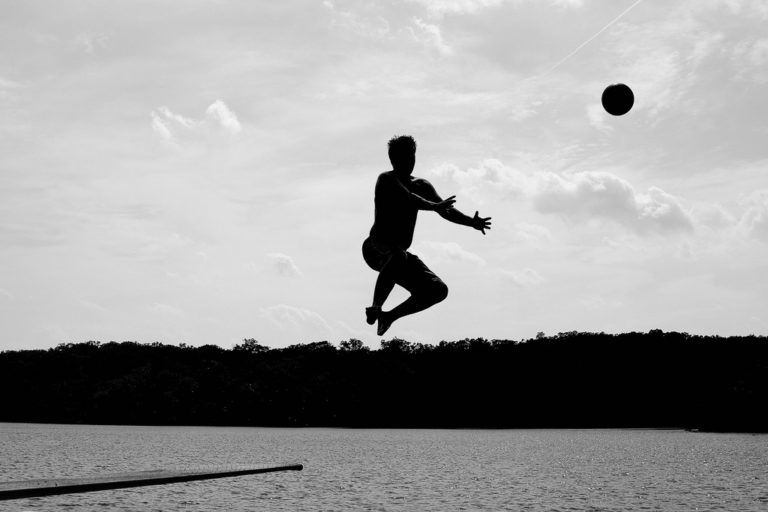 man jumping into lake reaching out to catch a ball as he's going down