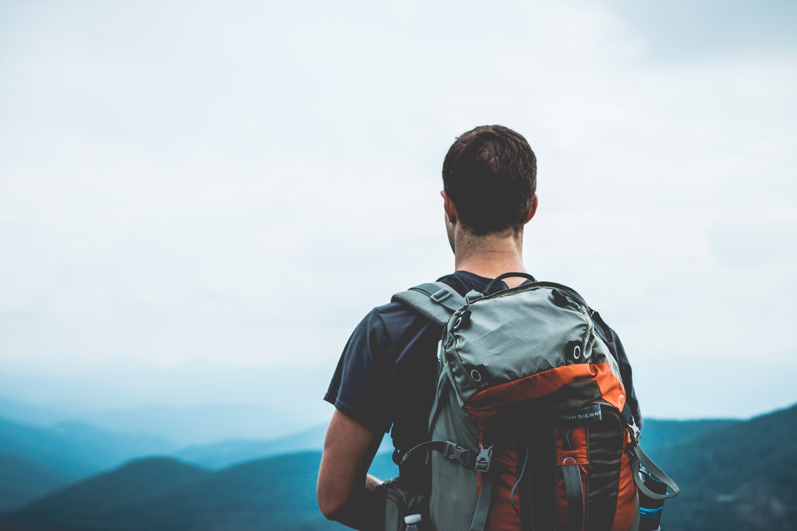 man looking out into beautiful mountainous scenery while wearing a backpack after a hike up to the top
