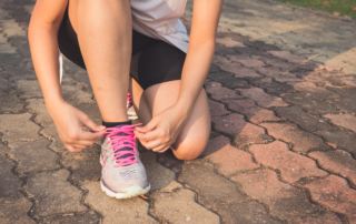 closeup of woman kneeling down to tie her sneaker while she's exercising outside