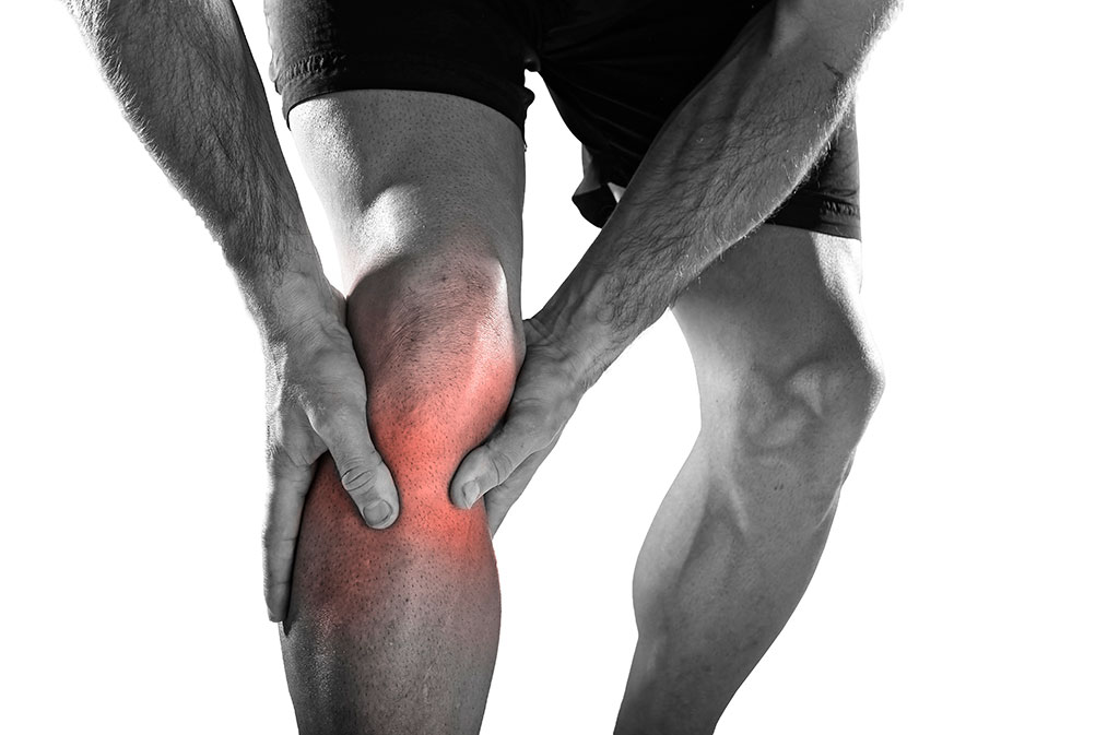 man holding his knee which is showing a red spot with a sports injury to the knee