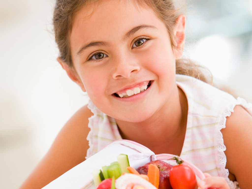 little girl smiling while holding a lunchbox of healthy food