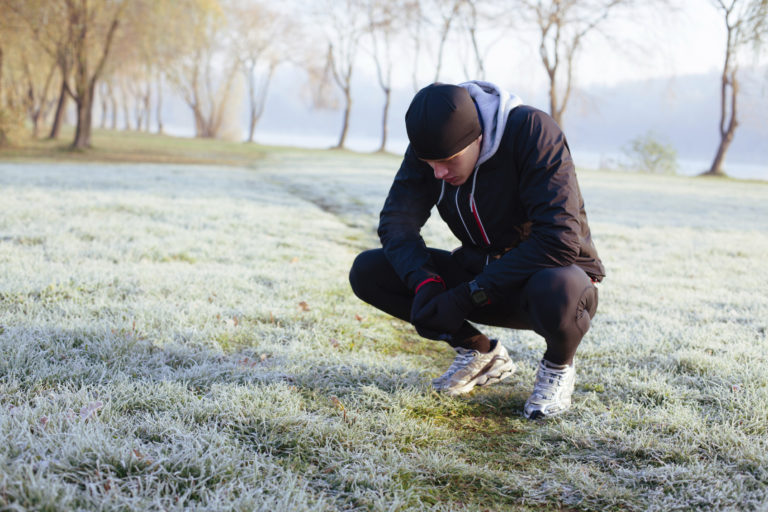 man bent over catching his breath after working out in the cold, fully bundled up with a warm hat on and gloves