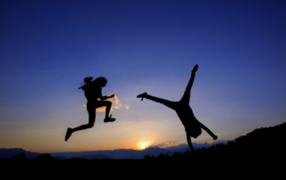 happy people jumping and doing cartwheels silhouette in front of sunset