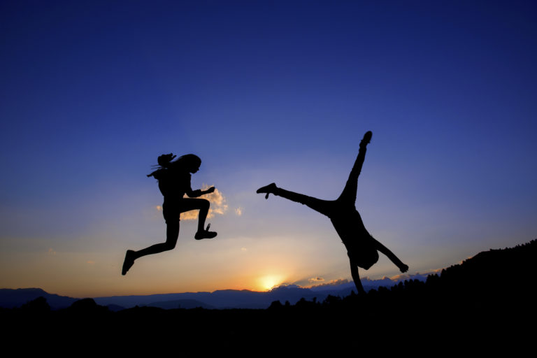 happy people jumping and doing cartwheels silhouette in front of sunset