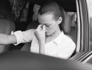woman sitting in her car pinching her nose to help reduce her stress headache
