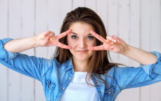 woman smiling at the camera holding her hands up in peace signs by her eyes