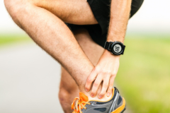 closeup of a runner holding his ankle mid run due to pain