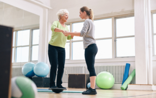 young female physical therapist working with an older female on a balancing ball during balance rehabilitation