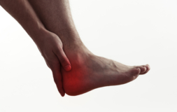 person holding their hand up against their ankle where a red light is covering the area of pain in their ankle