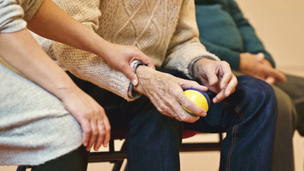 closeup of senior-age man holding a ball while the physical therapist directs his arm during hand relief therapy