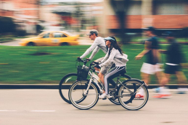 couple riding bikes together in a city setting zooming past people who are walking