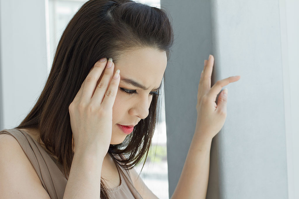 woman holding her head with one hand and using her other hand to lean up against the wall because she's experiencing vertigo