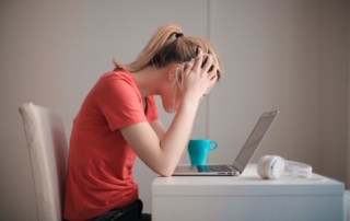 woman sitting in front of her computer with hands running through hair expressing stress