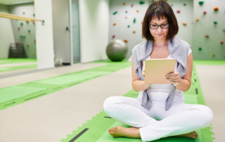 woman in physical therapy researching annual insurance deductible, sitting on green mat surrounded by green climbing walls