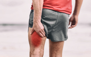 man holding his left hamstring with a red spot signaling pain and in need of muscle pain treatment
