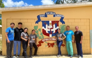 momentum physical therapists standing in front of yellow building with blue and red shield logo on the wall